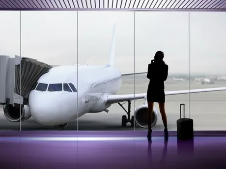 O pasageră așteaptă la aeroport, privind un avion pe pistă.