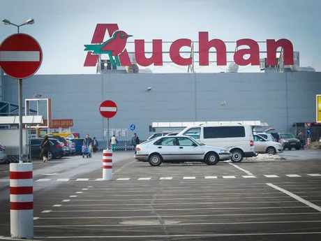 Exteriorul unui magazin Auchan, cu parcarea plină de mașini.