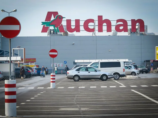Exteriorul unui magazin Auchan, cu parcarea plină de mașini.