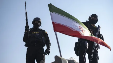 Soldați iranieni în fața steagului național, pregătiți pentru acțiune.