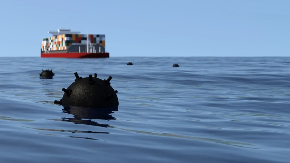 Mine marine sub apă, cu un vas de marfă în fundal, pe o apă calmă.