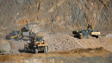 Activități de minerit în peisaj montan, cu utilaje grele în acțiune.