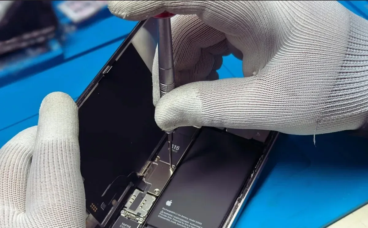 Un tehnician înlocuiește bateria unui smartphone pe un birou de lucru.