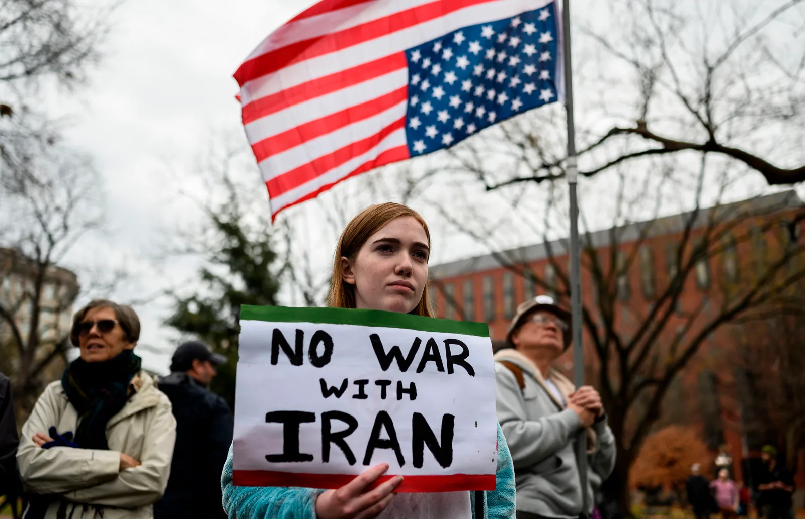 Protest împotriva războiului cu Iranul, cu steagul american în fundal.