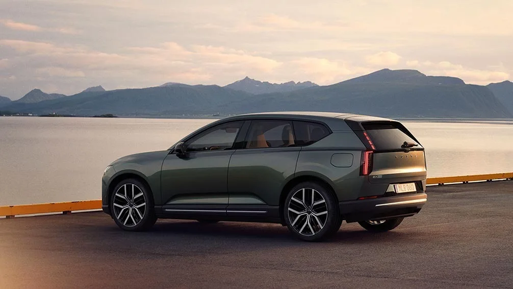 Volvo EX60 parcat pe malul unui lac, cu munți în fundal.