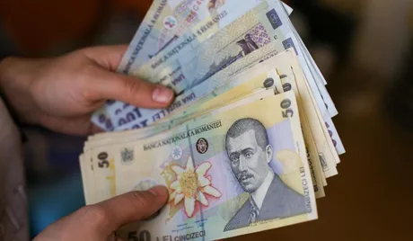 Bancnote românești în mână, simbolizând salariile restante.