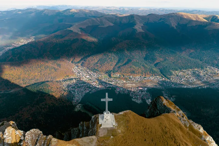 Peisaj montan spectaculos cu crucea de pe vârful muntelui.