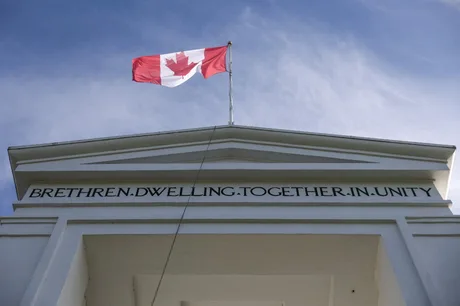 Clădire cu steagul Canadei fluturând pe fondul cerului senin.