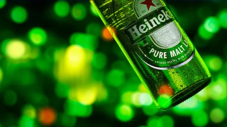 Sticlă de bere Heineken pe fundal verde, simbolizând schimbările din companie.