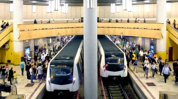 Stație de metrou aglomerată, cu trenuri și călători în mișcare.