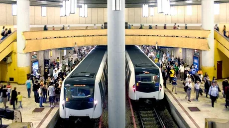 Stație de metrou aglomerată, cu trenuri și călători în mișcare.