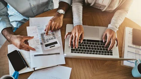 Persoane analizând documente financiare și folosind un calculator.