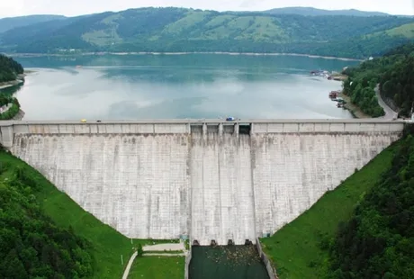 Barajul de la Ipotești, pe fundalul lacului de acumulare, într-un peisaj verde.
