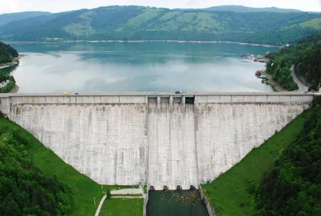 Barajul de la Ipotești, pe fundalul lacului de acumulare, într-un peisaj verde.