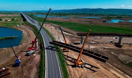 Lucrări de construcție pe Autostrada A7, cu utilaje și peisaj verde.