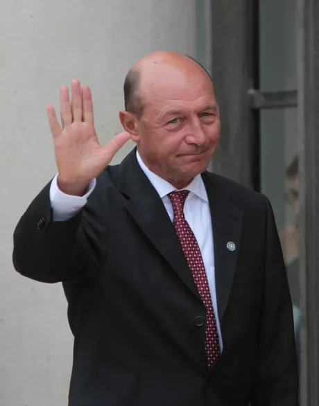 Traian Băsescu salută, purtând un costum elegant.