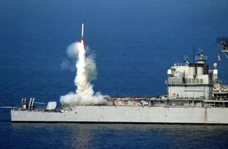 Lansare de rachetă de pe o navă militară în apă, cu fum și apă în jur.