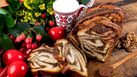 Cozonaci delicioși pe masă, alături de flori și ouă roșii.