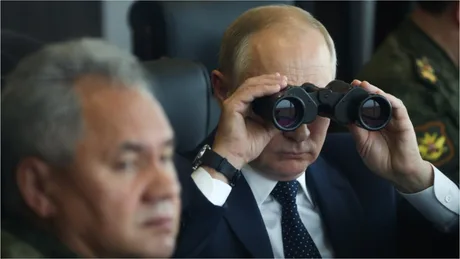 Vladimir Putin observând cu binoclu, într-un context militar.