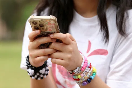 Un copil folosește telefonul mobil, purtând brățări colorate pe încheietură.