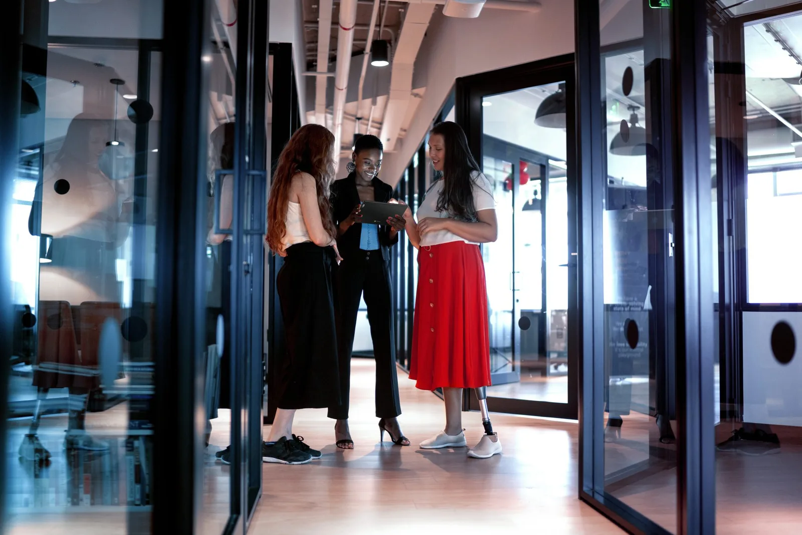 Trei femei discută într-un birou modern, înconjurate de sticlă și lumină naturală.