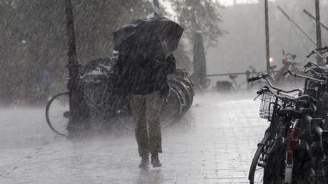 Persoană protejată cu umbrelă pe o stradă plină de apă în timpul unei furtuni.