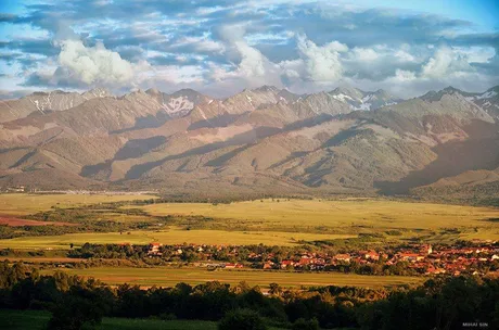 Peisaj montan cu văi verzi și sate pitorești în fundal.