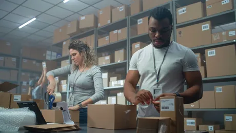 Angajați ambalând produse într-un depozit plin de cutii.