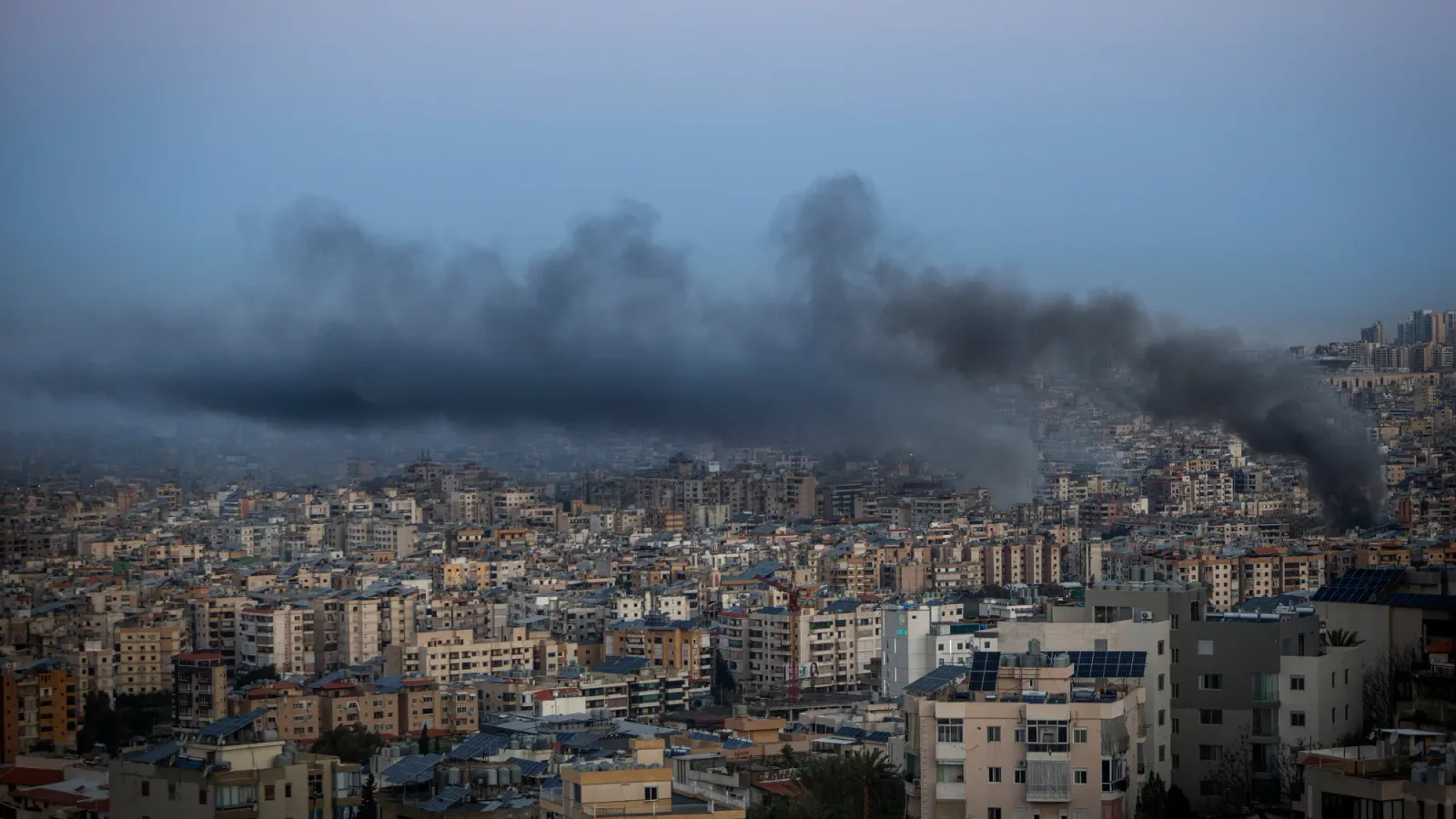 Fum negru se ridică deasupra unui oraș dens populat, semn al unor atacuri recente.