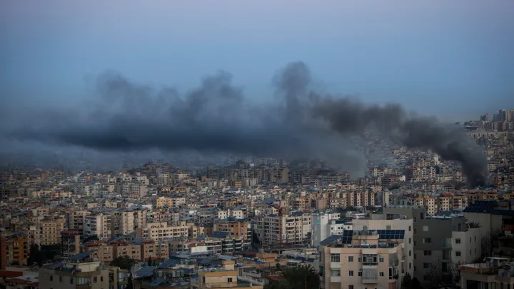 Fum negru se ridică deasupra unui oraș dens populat, semn al unor atacuri recente.