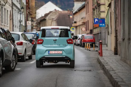 Un vehicul electric CityZEN circulând pe o stradă din Brașov, printre mașini parcate.