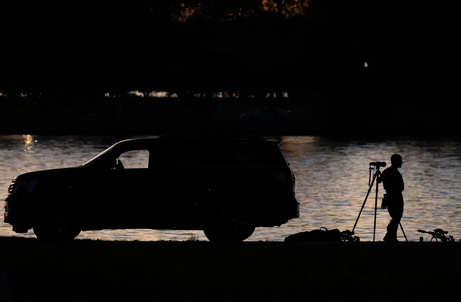 Un vehicul parcat lângă apă, cu o siluetă umană în fundal.