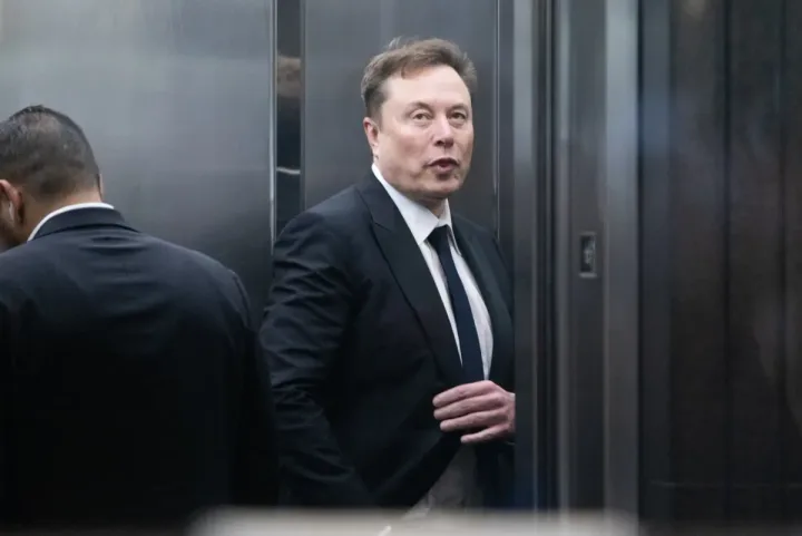 Elon Musk într-un lift, îmbrăcat elegant, discutând despre AI.
