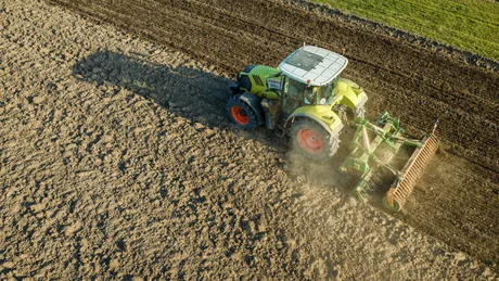 Tractor lucrând pe un câmp pregătit pentru semănat.