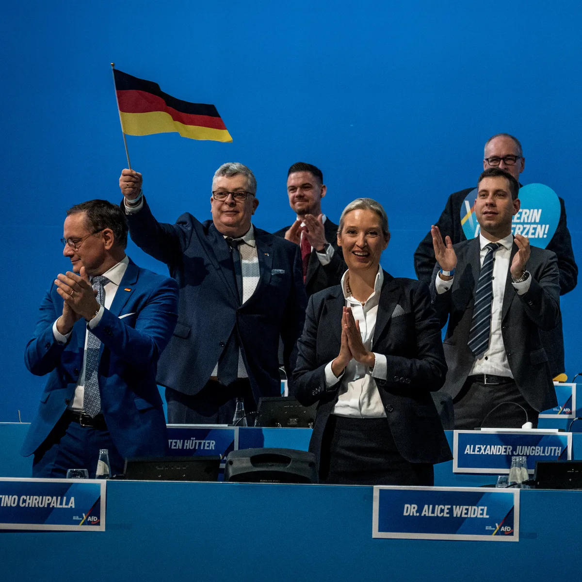 Susținători ai AfD la o conferință, cu steagul Germaniei în mână.