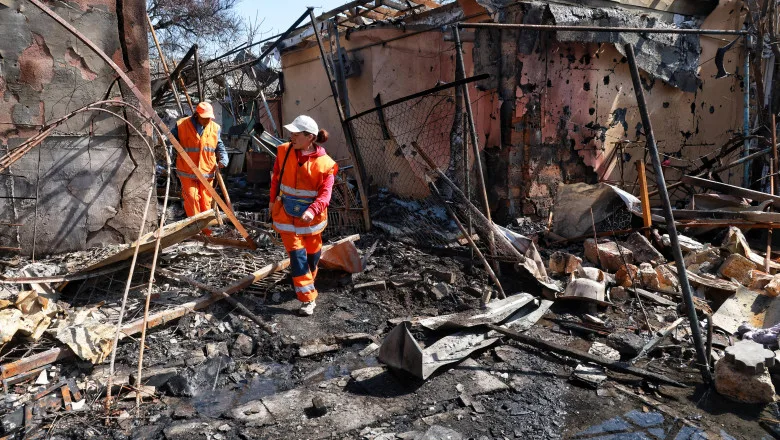 Doi lucrători inspectează ruinele unei clădiri distruse de atacuri aeriene.