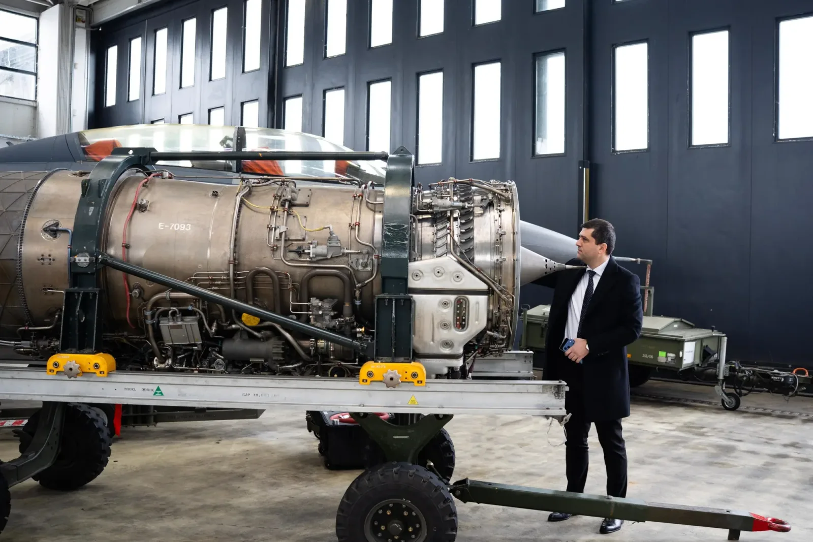 Un bărbat inspectează un motor într-un hangar industrial.