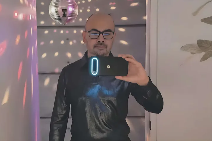 Un bărbat își face selfie cu un telefon în lumina unui discobol.