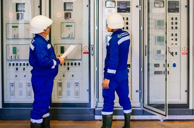 Specialiști analizând echipamente electrice într-o stație de distribuție.