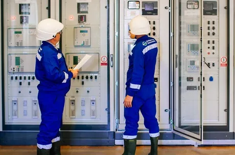 Specialiști analizând echipamente electrice într-o stație de distribuție.