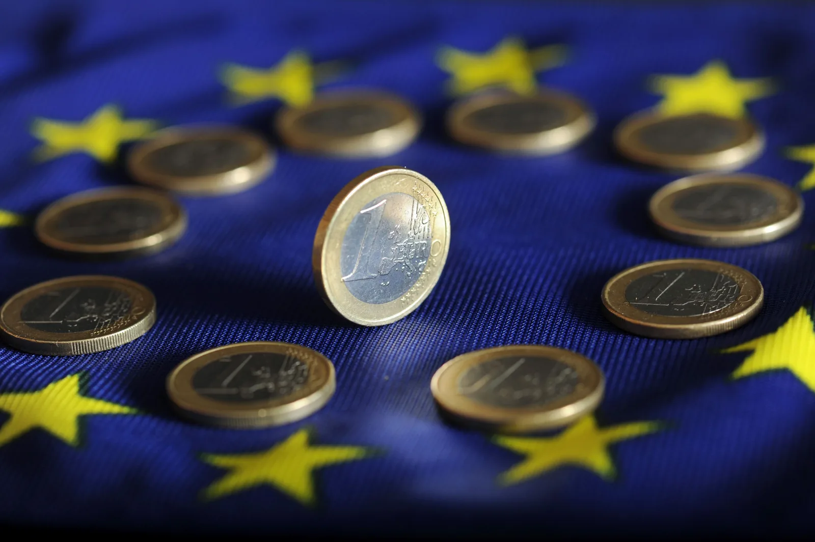 Monede euro pe fundalul steagului Uniunii Europene, simbolizând integrarea economică.