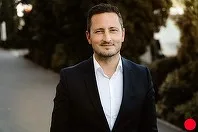 Mircea Abrudean zâmbește, îmbrăcat elegant, pe fundal verde.