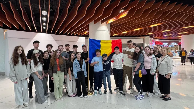 Grup de români repatriați din Oman, cu steagul României în fundal.