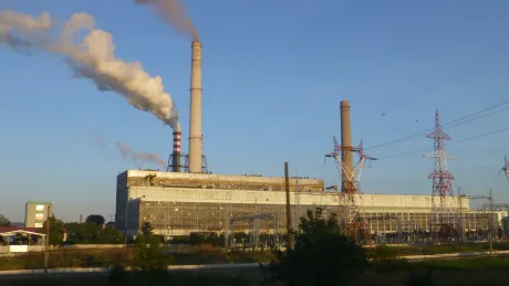 Centrala pe cărbune cu fum ieșind din coșuri, pe fundal cer senin.