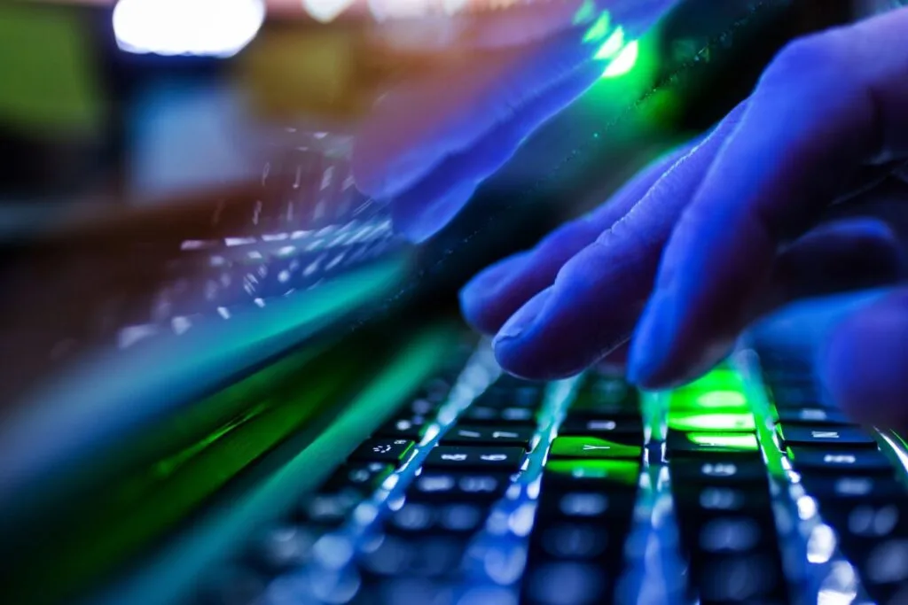 Mâini care tastează pe un keyboard iluminat, simbolizând spionajul cibernetic.