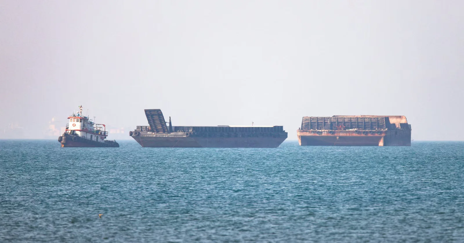 Nave comerciale ancorate în apă, cu un peisaj maritim neclar în fundal.