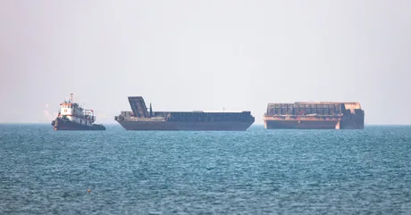 Nave comerciale ancorate în apă, cu un peisaj maritim neclar în fundal.