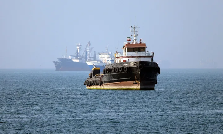 Vapor maritim navigând pe ape calme, cu nave în fundal.