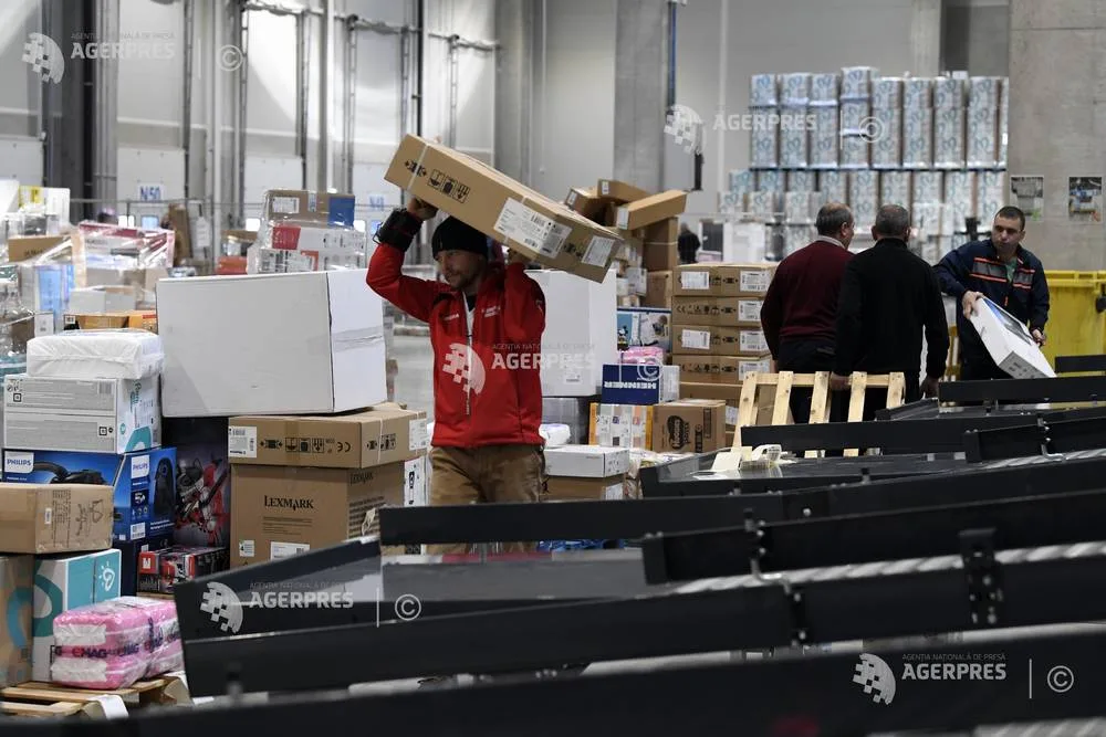 Un muncitor transportă cutii într-un depozit aglomerat.