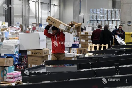 Un muncitor transportă cutii într-un depozit aglomerat.